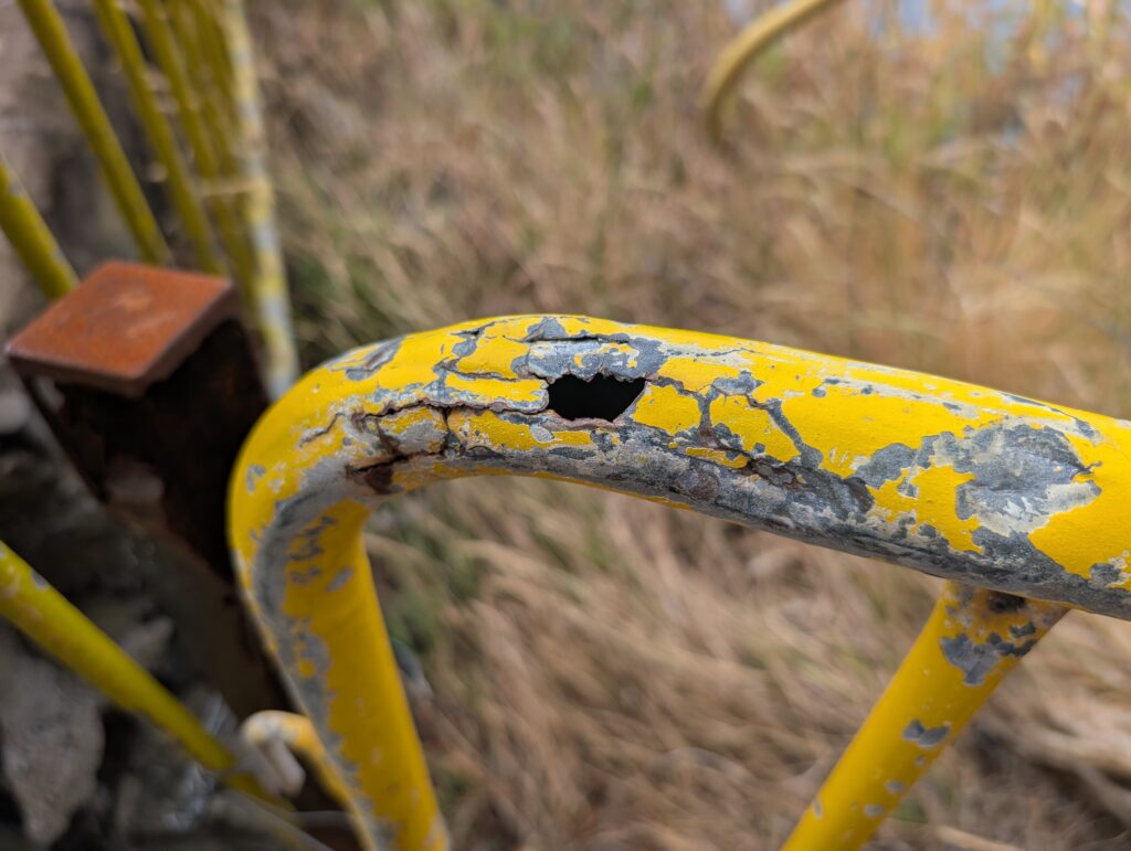 Yellow painted carbon steel tube handrail with through-wall corrosion perforation, Madeira Portugal